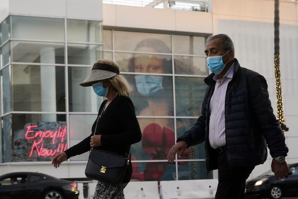 FILE - In this Dec. 9, 2020, file photo, masked pedestrians walk past of a COVID 19-themed mural depicting Leonardo da Vinci's Mona Lisa in Beverly Hills, Calif. The first COVID-19 vaccinations are underway at U.S. nursing homes, where the virus has killed upwards of 110,000 people, even as the nation struggles to contain a surge so alarming that California is dispensing thousands of body bags and lining up refrigerated morgue trailers. (AP Photo/Marcio Jose Sanchez, File)