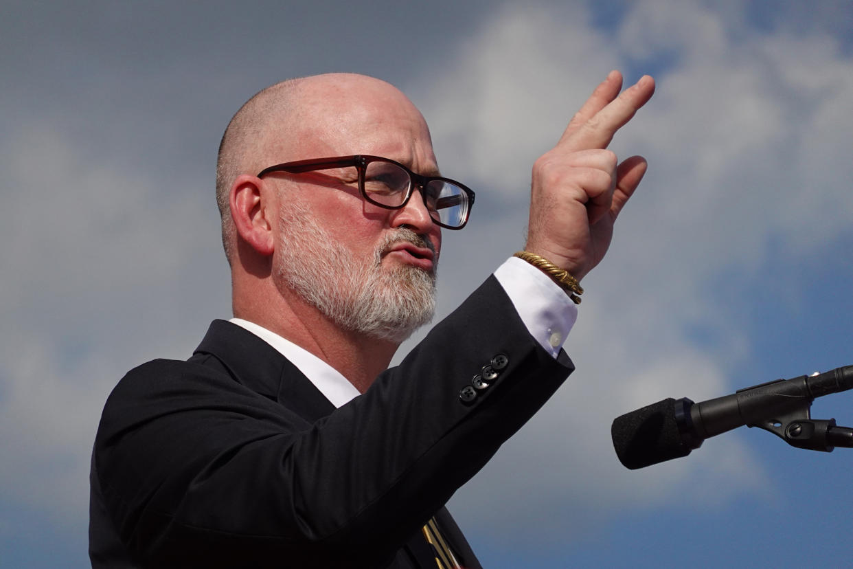 Derrick Van Orden at the microphone, wearing a suit jacket and white cuffs.