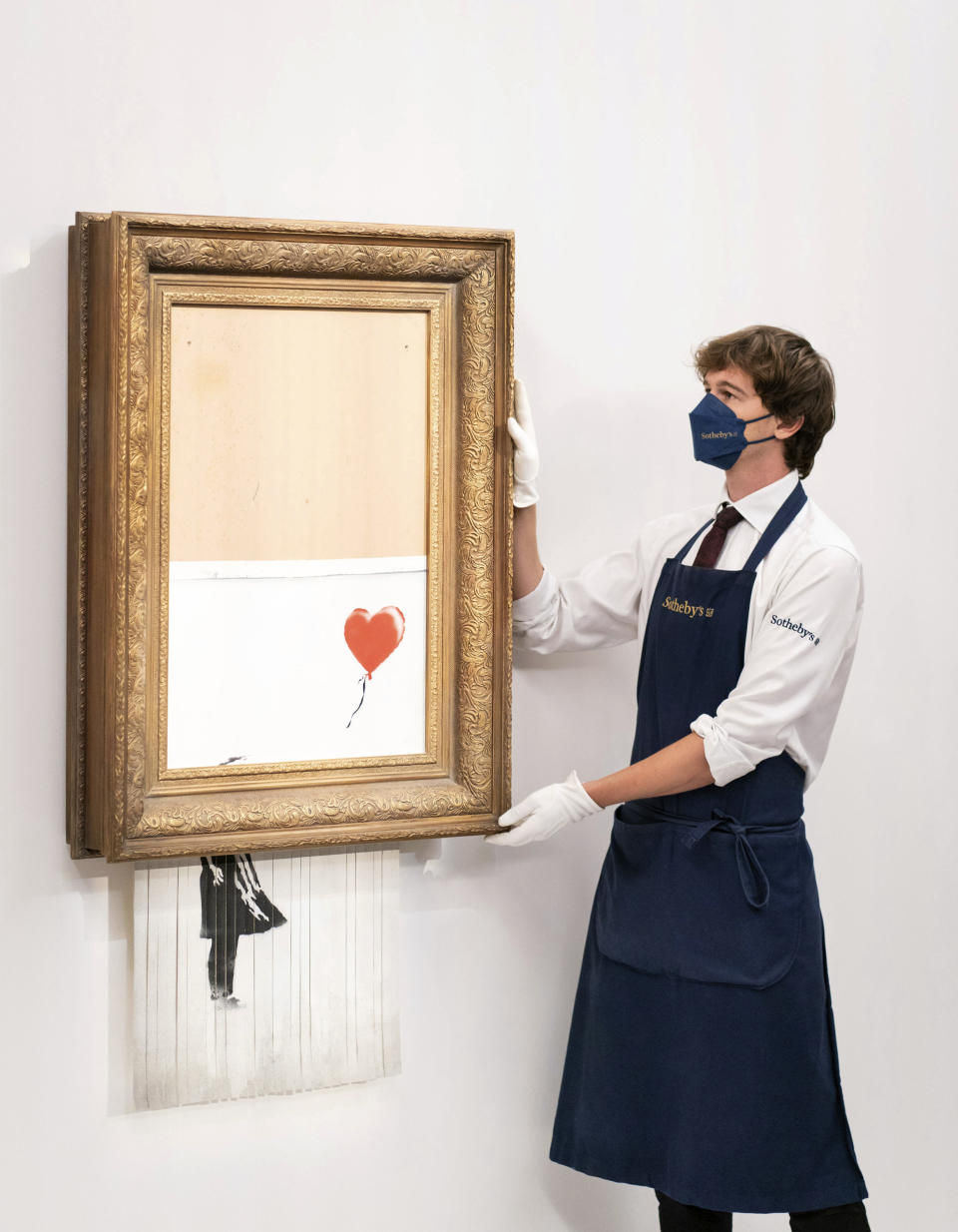 ARCHIVO - En esta foto del 3 de septiembre de 2021, un manipulador de arte sostiene "Love is in the Bin" de Banksy en la casa de subastas Sotheby's en Londres. La obra, que se autodestruyó de manera sensacional justo después de venderse por 1,4 millones de dólares, se ofrece de nuevo en subasta el jueves 14 de octubre con un precio de venta estimado en 4 a 6 millones de libras esterlinas (5,5 a 8,3 millones de dólares). (Dominic Lipinski/PA vía AP)