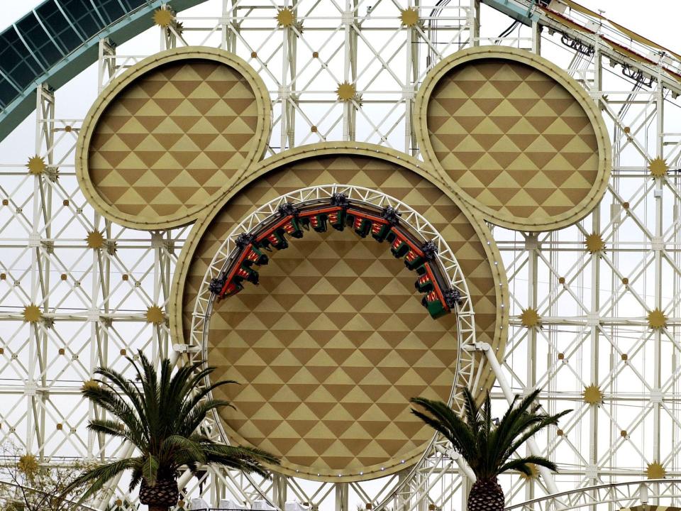 A rollercoaster with a giant Mickey Mouse head-shaped structure and tracks that loop in front of it. Cars and people are riding upside down in the loop.