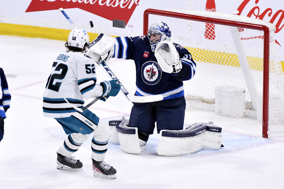 Winnipeg Jets goaltender Connor Hellebuyck, right, makes a save against San Jose Sharks' Tristen Robins (52) during third-period NHL hockey game action in Winnipeg, Manitoba, Monday April 10, 2023. (Fred Greenslade/The Canadian Press via AP)