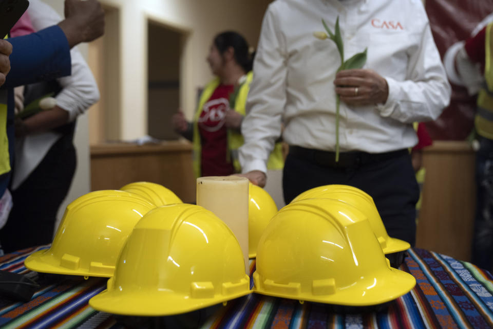 Construction workers and supporters gather around six construction helmets and a candle at a vigil and press conference by CASA of Maryland, a community advocacy group, to remember the six workers killed in the collapse of the Francis Scott Key Bridge and to highlight the difficult conditions faced by immigrant construction workers on Friday, March 29, 2024, in Baltimore, Md. (AP Photo/Mark Schiefelbein)