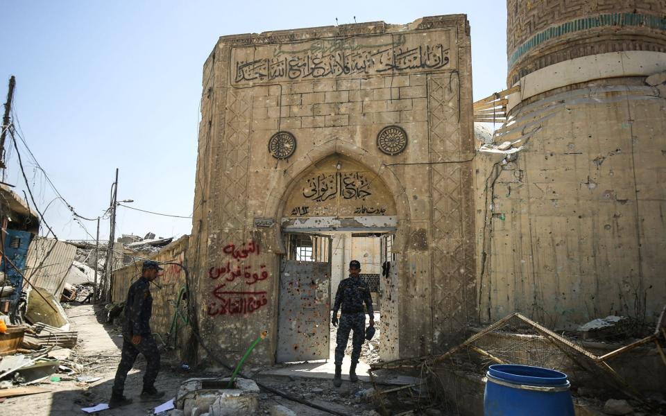 A member of the Iraqi federal police stands through the doorway leading into the damaged historic 19th cetnury Ziwani mosque in the Old City of Mosul - Credit: AFP