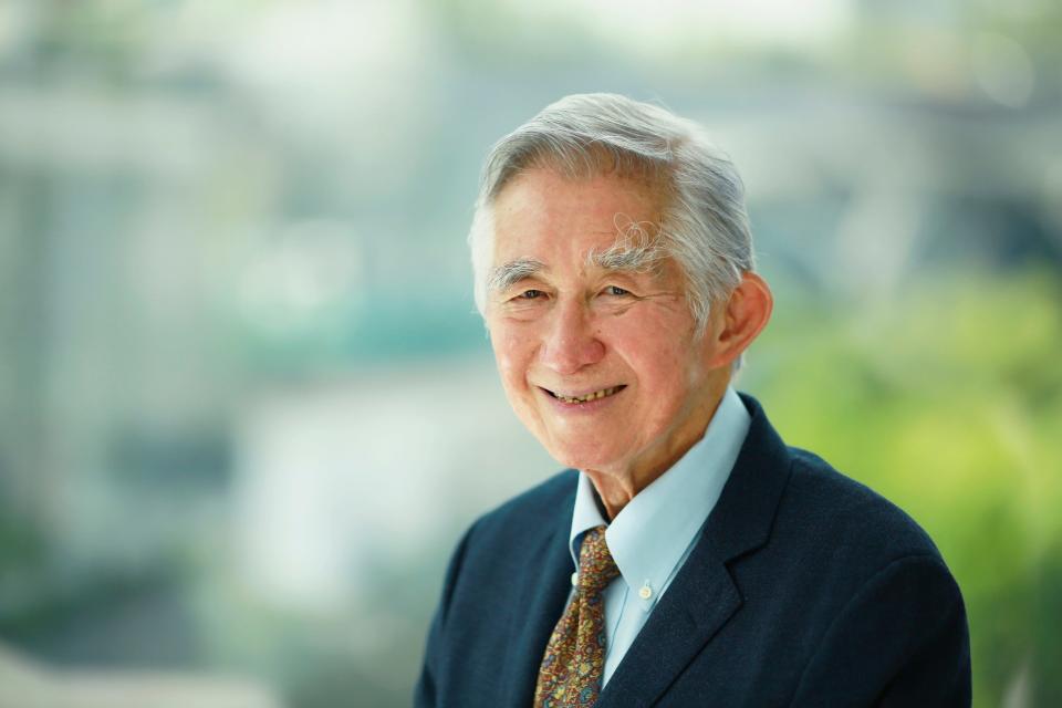 An older Asian man with white hair and a suit smiling for the camera.