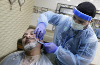 A barber wears a protective face shield and gloves to help curb the spread of the coronavirus, as he shaves the beard of a customer at a local barber shop in Jiddah, Saudi Arabia, Sunday, June 28, 2020. (AP Photo/Amr Nabil)