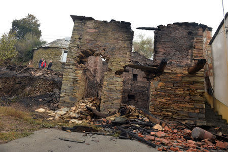 People stand next to a house burnt by forest fire in San Martin de Cereixedo, Cervantes, Galicia, northern Spain October 17, 2017. REUTERS/Vincent West