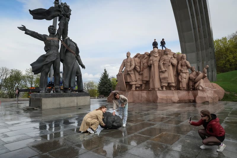 People take pictures of a Soviet monument to a friendship between Ukrainian and Russian nations during its demolition in central Kyiv