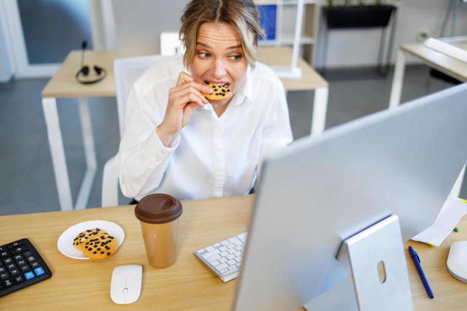 Business woman in a hurry is forced to snack on cookies while working at the computer