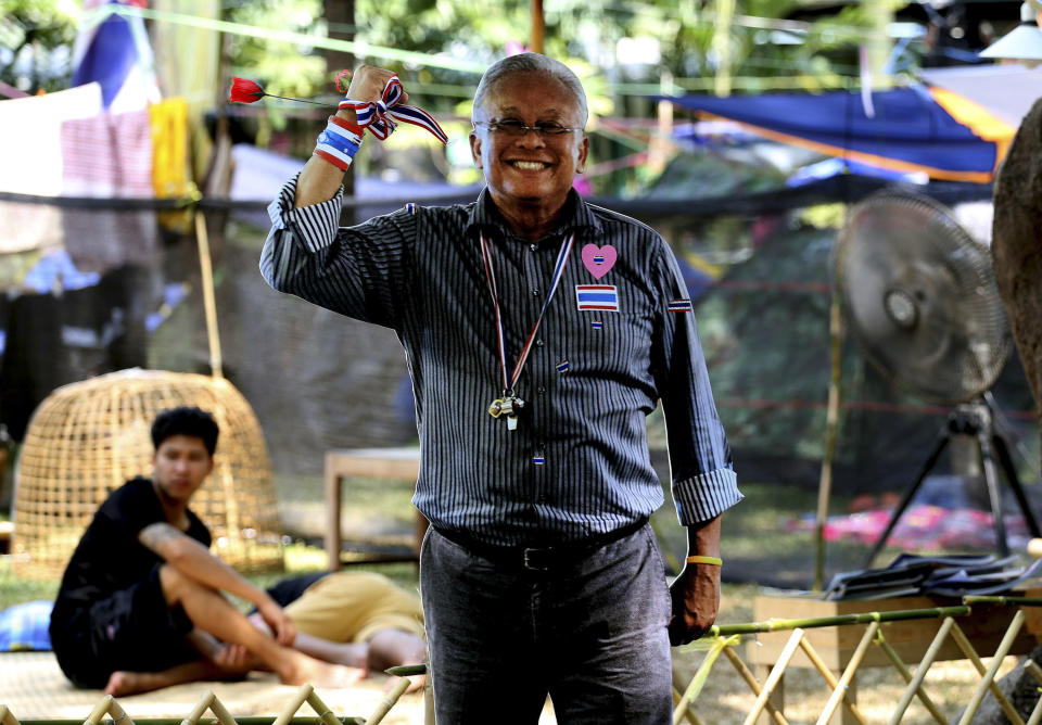 An anti-government protester, left, sits near a life-sized cut-out board of protest leader Suthep Thaugsuban erected at an encampment inside Lumpini park in Bangkok, Thailand Tuesday, March 18, 2014. Thailand’s government is lifting a state of emergency in Bangkok and surrounding areas after violence related to the country’s political crisis eased. (AP Photo/Apichart Weerawong)