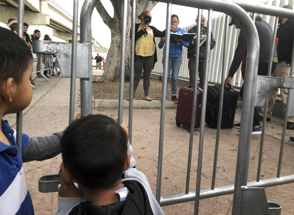 Two Mexican boys in Tijuana, Mexico, listen to volunteers calling names from a waiting list to claim asylum in the U.S. at a border crossing in San Diego, Thursday, Sept. 26, 2019. The Trump administration played "bait and switch" by instructing migrants to wait in Mexico for an opportunity to apply for asylum before imposing sharp restrictions on eligibility, attorneys said in a court filing Thursday. (AP Photo/Elliot Spagat)