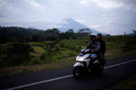 People ride a motorcycle past Mount Agung in the background, a volcano on the highest alert level, in Karangasem Regency, on the resort island of Bali, Indonesia, September 24, 2017. REUTERS/Darren Whiteside