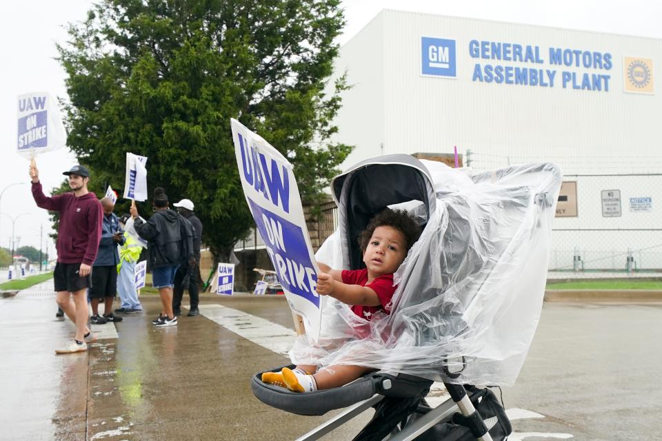 Auhsten Bartlett, 18 months old, holds a sign while his parents Edward Bartlett, not visible, a General Motors trim department employee, and Trista Bartlett picket with others outside the company's assembly plant, Tuesday, Oct. 24, 2023, in Arlington, Texas.