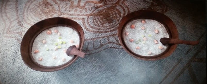 The two brown bowls of shrimp congee each have a wooden spoon in them