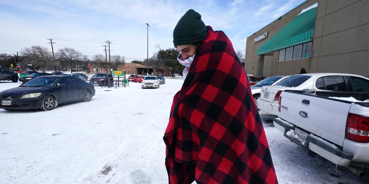 Cody Jennings uses a blanket to keep warm outside a grocery store Tuesday, Feb. 16, 2021, in Dallas.