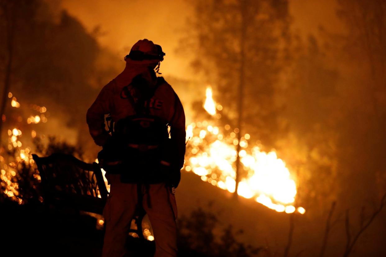 A firefighter watches flames advance up a hill towards homes as crews battle the Carr Fire, west of Redding, California