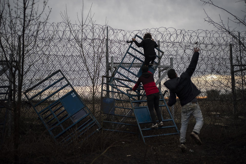 A migrant, right, throws a stone to the Greek riot police as other two migrants climbing on a border fence at the Turkish-Greek border in Pazarkule, Edirne region, Turkey, on Friday, March 6, 2020. Clashes erupted anew on the Greek-Turkish border as migrants attempted to push through into Greece, while the European Union's foreign ministers held an emergency meeting to discuss the situation on the border and in Syria, where Turkish troops are fighting. (AP Photo/Felipe Dana)