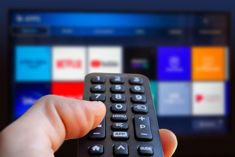 Hand holding a remote control aimed at a blurred television screen with various app icons