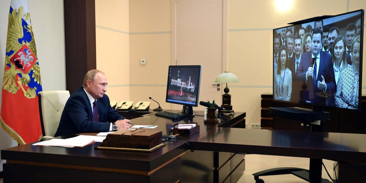 President Vladimir Putin sits behind a desk, facing a videoconferencing screen showing graduates of RANEPA university on August 20, 2020.