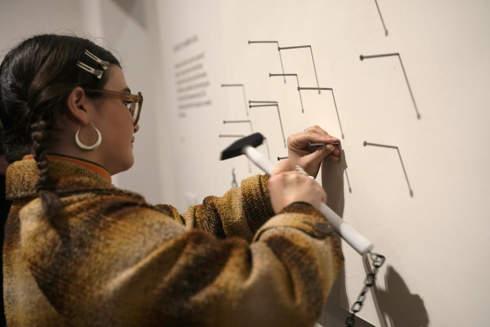 A member of staff participates in the Painting of a Hammer a Nail, Concept 1961, exhibition realisation 2024, which is viewer interactive at the Yoko Ono : Music of the Mind exhibition at the Tate Modern, the works of art are copyright Yoko Ono, in London, Tuesday, Feb. 13, 2024. The exhibition which has many pieces that are interactive and the public and participate in, runs from Feb.15, to Sept. 1. (AP Photo/Alastair Grant)