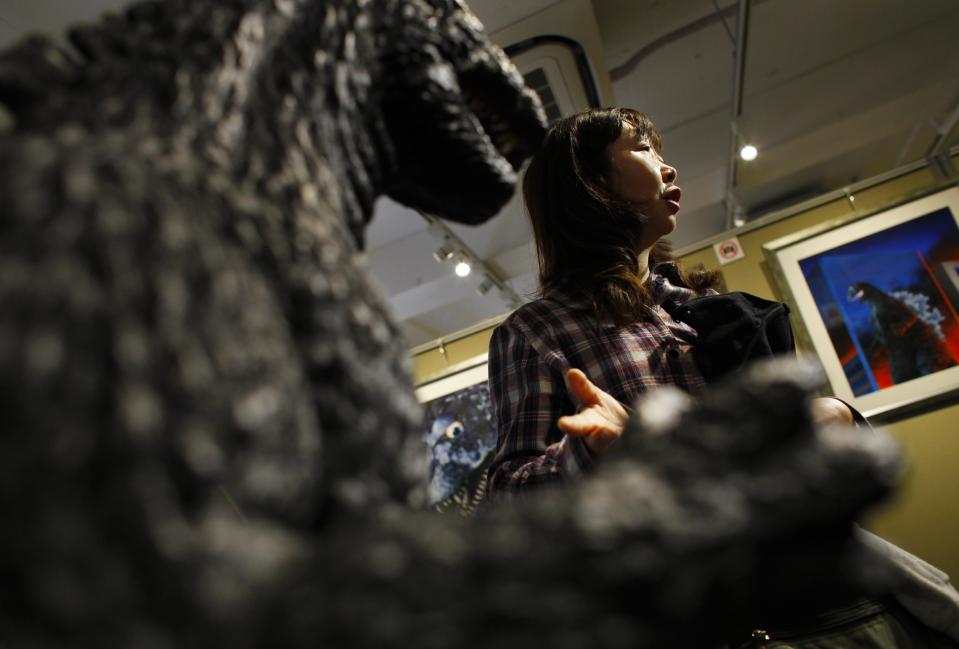 In this Monday, April 28, 2014 photo, a visitor to the gallery to showcase art painting of Godzilla by Yuji Kaida, Yumiko Yamashita stands near a large figure of Godzilla on display at Cheepa's gallery in Tokyo. Yamashita, a 40-year-old welfare-worker, thinks Godzilla must be lovable - “kawaii” is the way she describes it. She is proud it’s drawing overseas respect but scoffed at U.S. depictions: “They make it too flashy. It becomes too American.” (AP Photo/Junji Kurokawa)