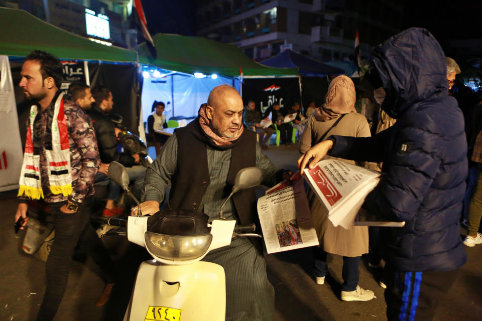 In this Tuesday, Nov. 19, 2019 photo, a masked man distributes copies of the "Tuk Tuk" newspaper, in Tahrir Square in Baghdad, Iraq. A small group of Iraqi volunteers is working in secrecy to produce the newspaper that aims to be the voice of the largest grassroots protest movement in the country’s modern history. Its editors say the newspaper is vital amid shutdowns of the internet, filling a void left by mainstream Iraqi journalists who either back the government or fear retaliation. (AP Photo/Khalid Mohammed)