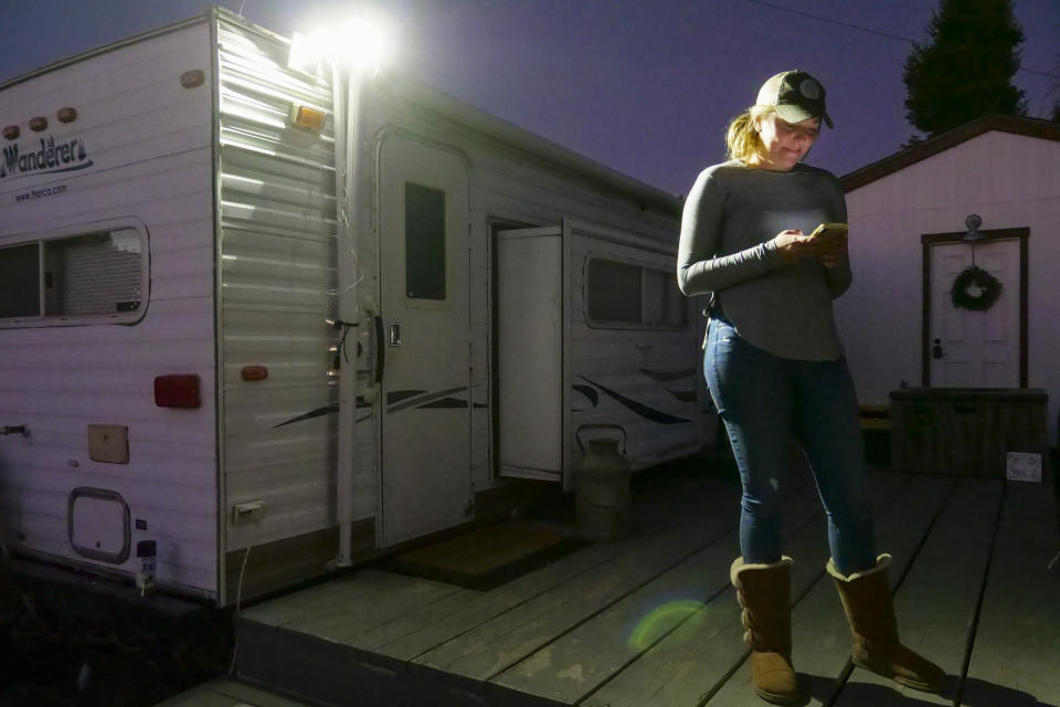 Jenna Chandler mira su teléfono el 4 de noviembre del 2019 junto al remolque donde está viviendo con su esposo Bobbie mientras construyen su casa en Santa Rosa, California. Los incendios forestales que destruyeron la casa de los padres de Bobbie en la misma calle no los amedrentan. (AP Photo/Lacy Atkins)