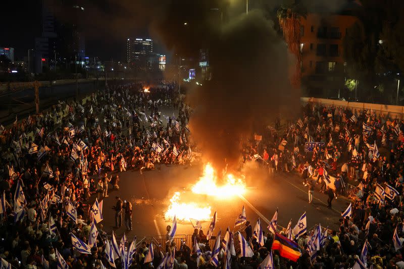 Arde fuego mientras la gente asiste a una manifestación después de que el primer ministro israelí, Benjamin Netanyahu, destituyera al ministro de Defensa y su Gobierno de coalición nacionalista siguiera adelante con su reforma judicial, en Tel Aviv, Israel