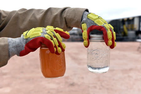 A worker holds up a jar of produced water (L) and recycled water (R) at a water recycling facility owned by Exxon near Carlsbad, New Mexico, U.S. February 11, 2019. Picture taken February 11, 2019. To match Insight USA-SHALE/MAJORS REUTERS/Nick Oxford