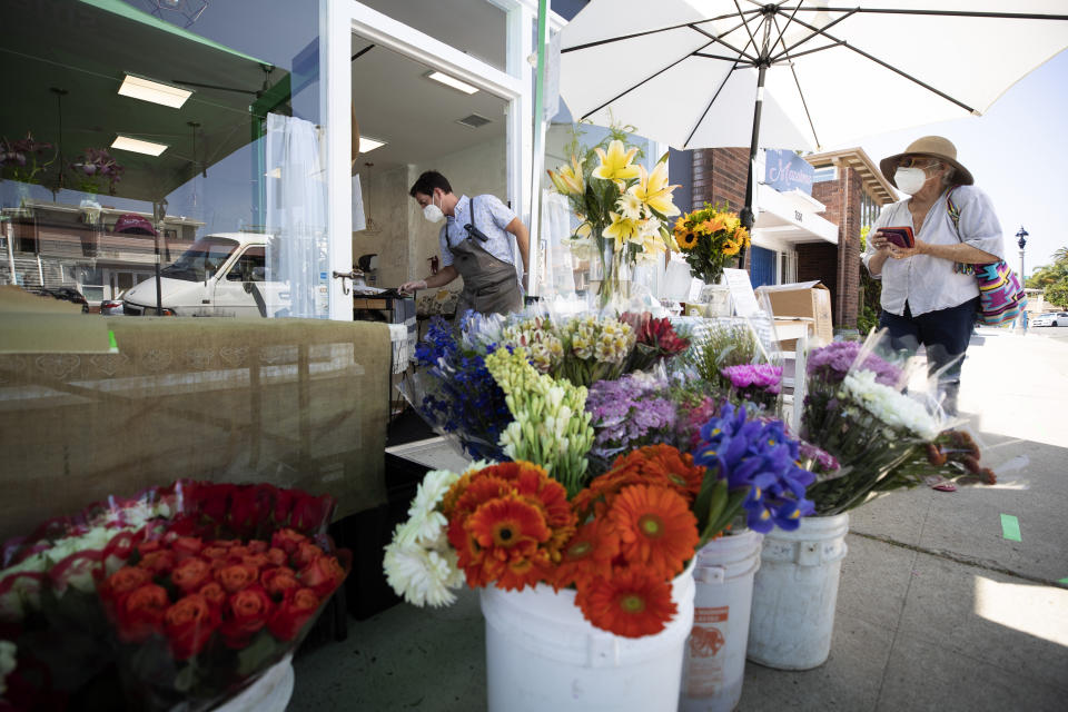 Mike Eastwood, center, rings up Mary Beebe, right, in front of his store, Smallgoods, Friday, May 8, 2020, in the La Jolla neighborhood of San Diego. Eastwood and his wife have adapted their new store to the changing economy of the pandemic by offering items from struggling farmers market vendors in the area alongside their own. California Gov. Gavin Newsom on Thursday issued the broadest loosening of his stay-at-home order so far, allowing retailers and manufacturers to reopen with new safety measures and setting strict criteria. (AP Photo/Gregory Bull)