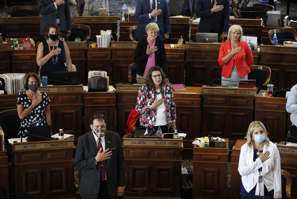 FILE - In this Wednesday, June 3, 2020 file photo, State Representatives stand at their desks during the Pledge of Allegiance in the Iowa House chambers, at the Statehouse in Des Moines, Iowa. The nation's ongoing battle against the coronavirus is dividing lawmakers along partisan lines in state Capitols. In some cases, the divisions can be seen simply by looking at lawmakers' faces. In some legislative chambers, many Democrats are wearing masks during debates while many Republicans are not. (AP Photo/Charlie Neibergall, File)