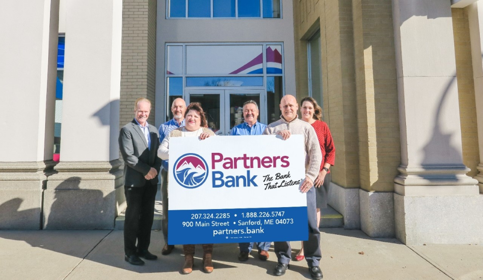 The Partners Bank Executive Team proudly presents the Partners Bank updated logo and accompanying designs in front of the bank’s Sanford, Maine headquarters. From left to right are Christopher Allen, Senior Vice President - Chief Risk Officer; Anthony Cataldi/Executive Vice President/Chief Operating Officer; Jennifer Stauffis, Senior Vice President/Chief Financial Officer; Blaine Boudreau, President/Chief Executive Officer; Sean O’Connell, Senior Vice President/Chief Information Officer; and Karyn Scharf Morin, Senior Vice President/Branch Administration.