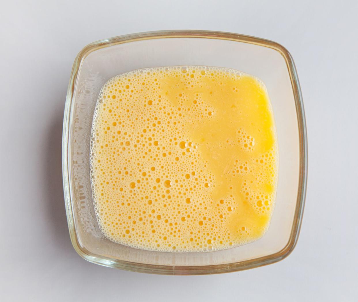 glass bowl of beaten eggs on grey kitchen table, top view