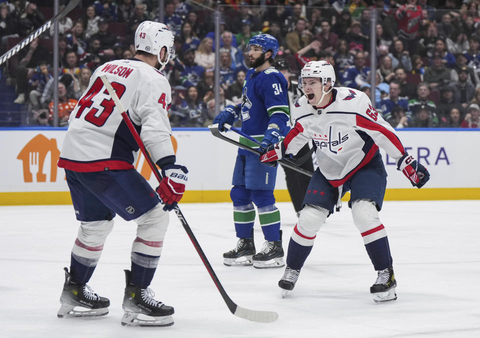 Washington Capitals' Ivan Miroshnichenko (63) and Tom Wilson (43) celebrate Wilson's goal as Vancouver Canucks' Phillip Di Giuseppe, back, skates past during the second period of an NHL hockey game in Vancouver, British Columbia, Saturday, March 16, 2024. (Darryl Dyck/The Canadian Press via AP)