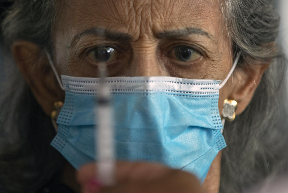 A woman eyes the syringe that will deliver her shot of the Sinovac COVID-19 vaccine at a drive-thru site set up in the Pacaembu soccer stadium parking lot during a priority vaccination program for seniors in Sao Paulo, Brazil, Wednesday, March 3, 2021. (AP Photo/Andre Penner)