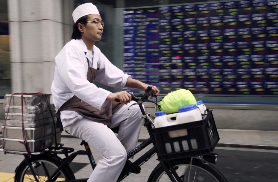 A man cycles past in front of electronic stock board of a securities firm in Tokyo, Tuesday, Sept. 25, 2018. Asian stock markets were mostly lower Tuesday after a Chinese government report accusing the Trump administration of bullying other countries dampened hopes for a settlement in their escalating tariff war. (AP Photo/Koji Sasahara)