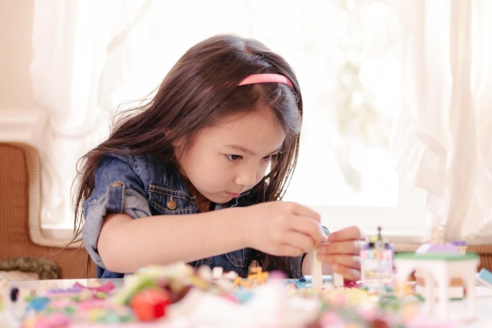 A young girl intently works on a LEGO set