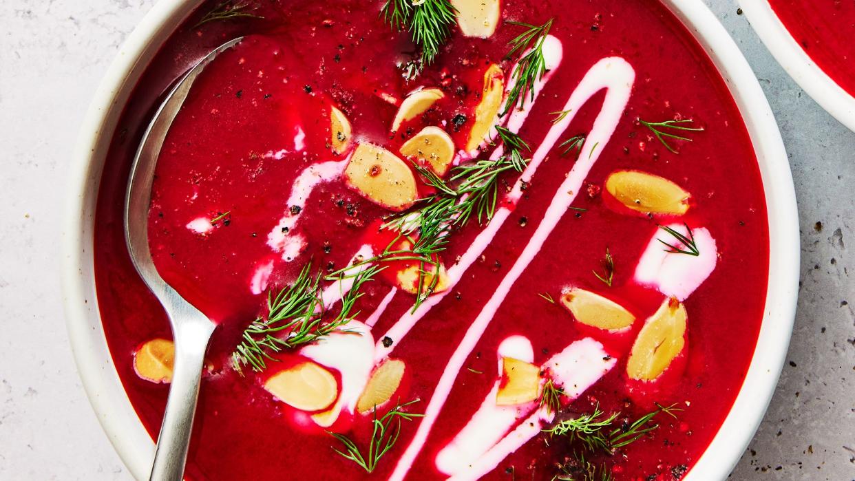 one pot harissa beet soup in a white bowl topped with almonds, herbs, and cream