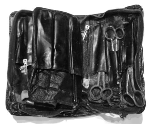 A weathered black leather barber kit holds several pairs of scissors and other instruments.