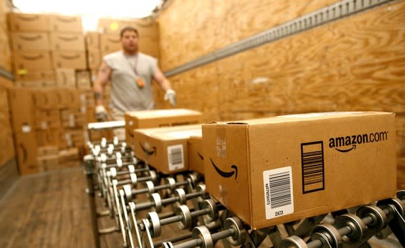 Amazon packages on a conveyer belt with a warehouse worker in the background
