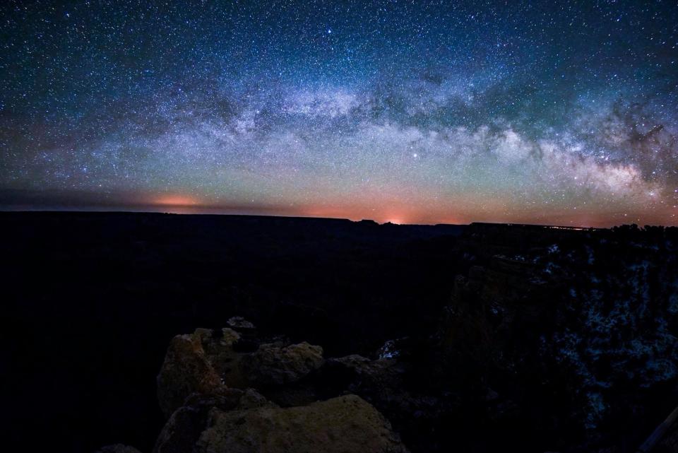 The Milky Way core stretches across the Grand Canyon, with the lights of towns of Tuba City and Kayenta light up the horizon.