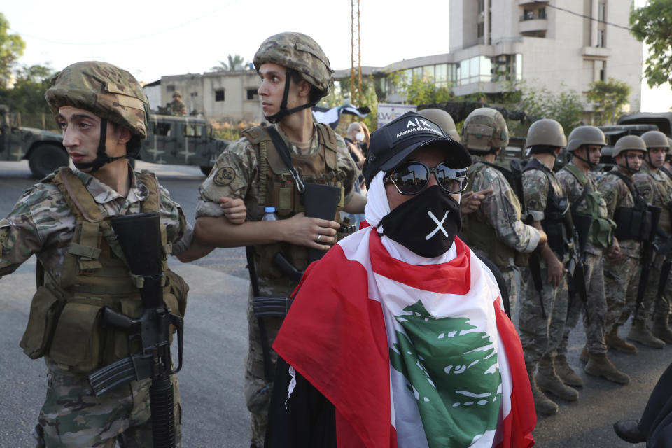 An anti-government protester stands in front Lebanese soldiers who block a road that links to the presidential palace, during a protest against the Lebanese President Michel Aoun, in Baabda east of Beirut, Lebanon, Saturday, Sept. 12, 2020. Soldiers fired rubber bullets and live rounds in the air to disperse hundreds of protesters trying to march to the presidential palace during an anti-government demonstration. (AP Photo/Bilal Hussein)