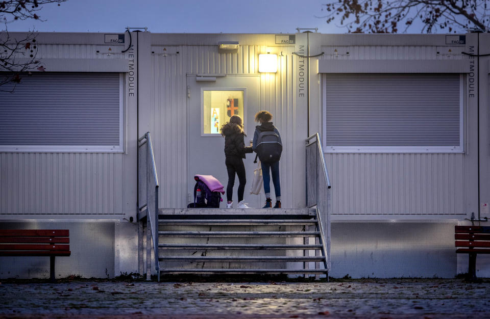 Pupils wait at a door of a school which is partially located in containers in Frankfurt, Germany, Monday, Dec. 14, 2020. Germany goes into a lockdown on Wednesday, Dec. 16, 2020. (AP Photo/Michael Probst)