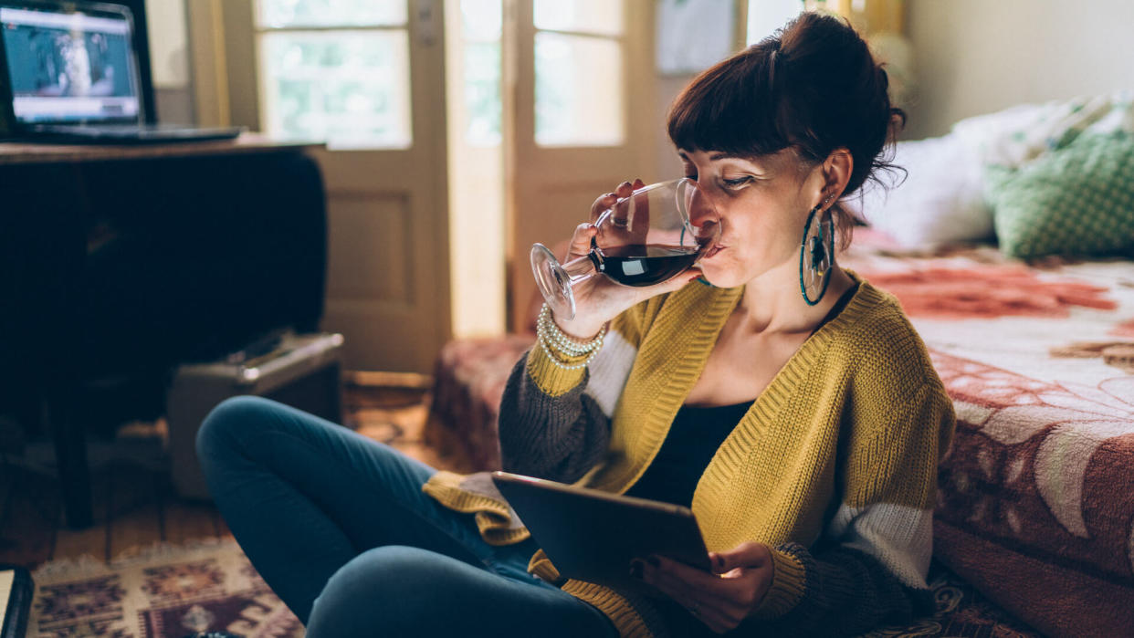 Young woman at home drinking red wine and using tablet.