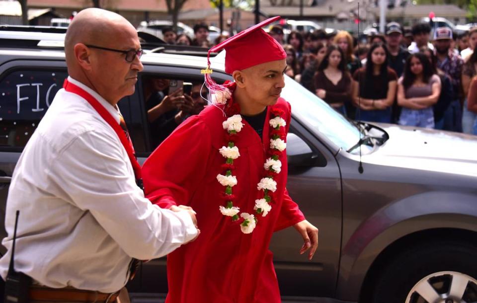 El director de Gustine High School, Adam Cano (izquierda), acompaña al estudiante de último año Brian Ortiz Núñez, en el trayecto desde su auto para aceptar su diploma durante una ceremonia especial de graduación celebrada el viernes 12 de abril de 2024 en Gustine High School.