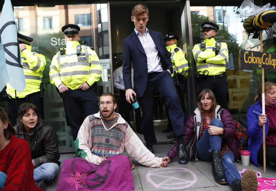 A man walks out of the Home office past climate change protesters on the second day of ongoing protests in London, Tuesday, Oct. 8, 2019. Police are reporting they have arrested more than 300 people at the start of two weeks of protests as the Extinction Rebellion group attempts to draw attention to global warming. (AP Photo/Alastair Grant)