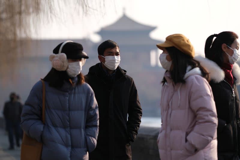 People wearing protective masks walk outside Forbidden City which is closed to visitors, according to a notice in its main entrance for the safety concern following the outbreak of a new coronavirus, in Beijing