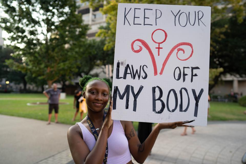 A woman smiles as she holds a sign: "Keep your laws off my body."