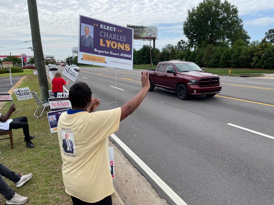 Bea Lyons, sister of Augusta Judicial Circuit superior court judge candidate Charles Lyons III, shouts and waves at traffic on Washington Road while campaigning for her brother in front of National Hills Baptist Church in Augusta, Ga., on May 24, 2022.