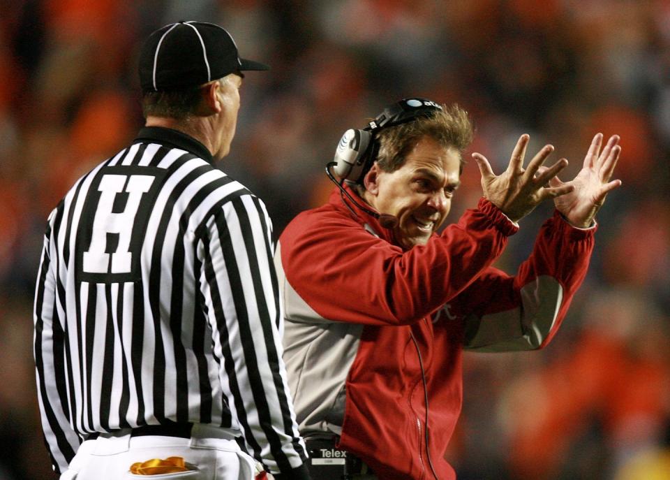 nick saban angrily yelling with his arms in the air as a referee looks on