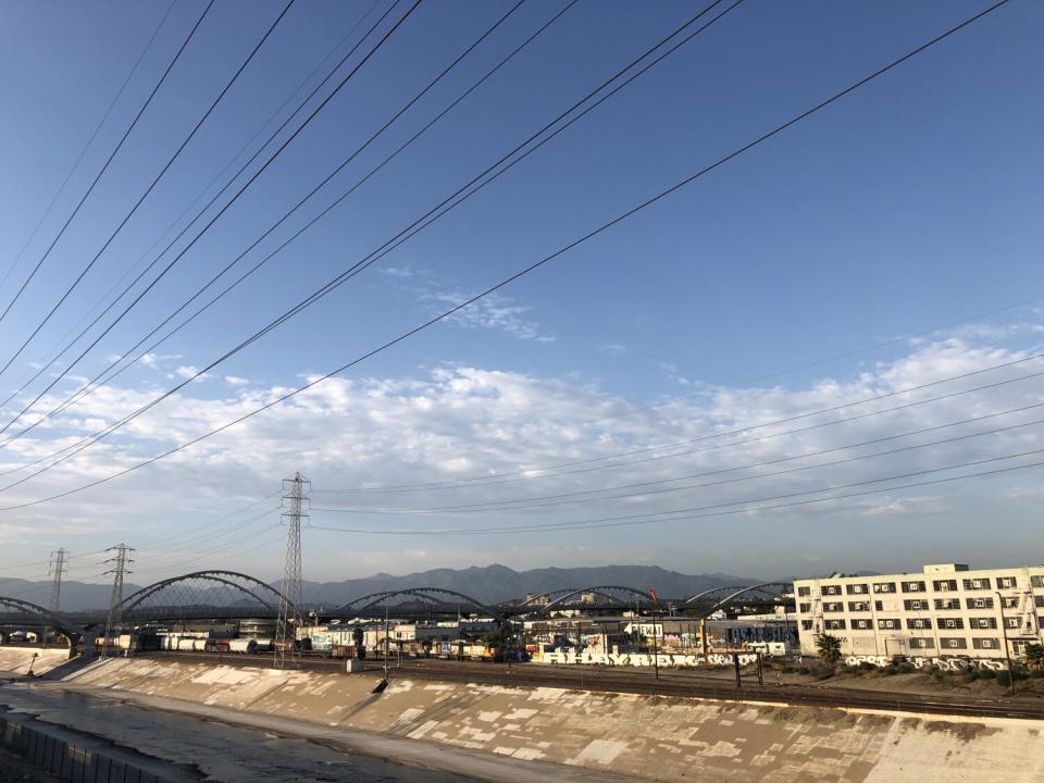 The arches of the 6th Street Bridge bound over the L.A. River and light industrial warehouses, with mountains as backdrop